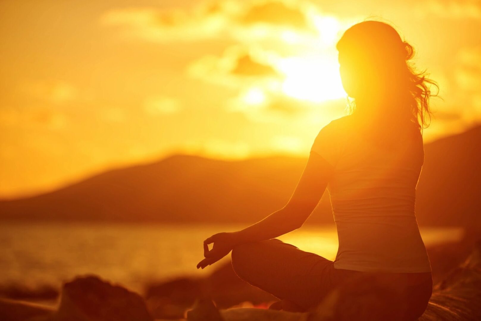 A person sitting in the sun with their hands in yoga pose.